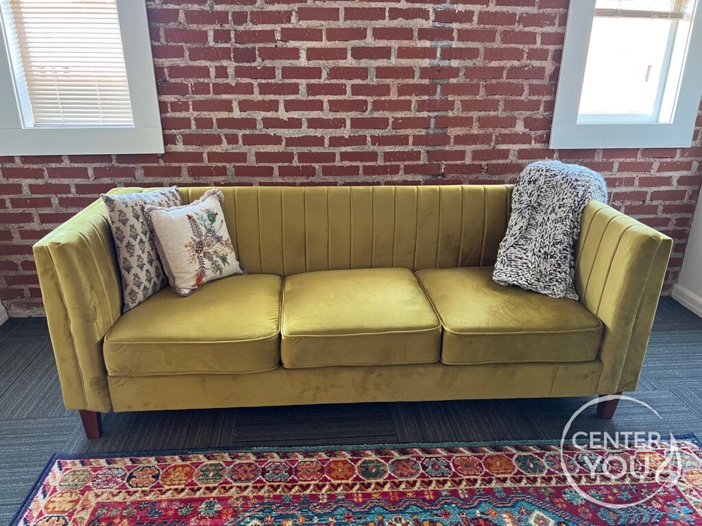 A yellow couch with pillows sitting against an interior brick wall.