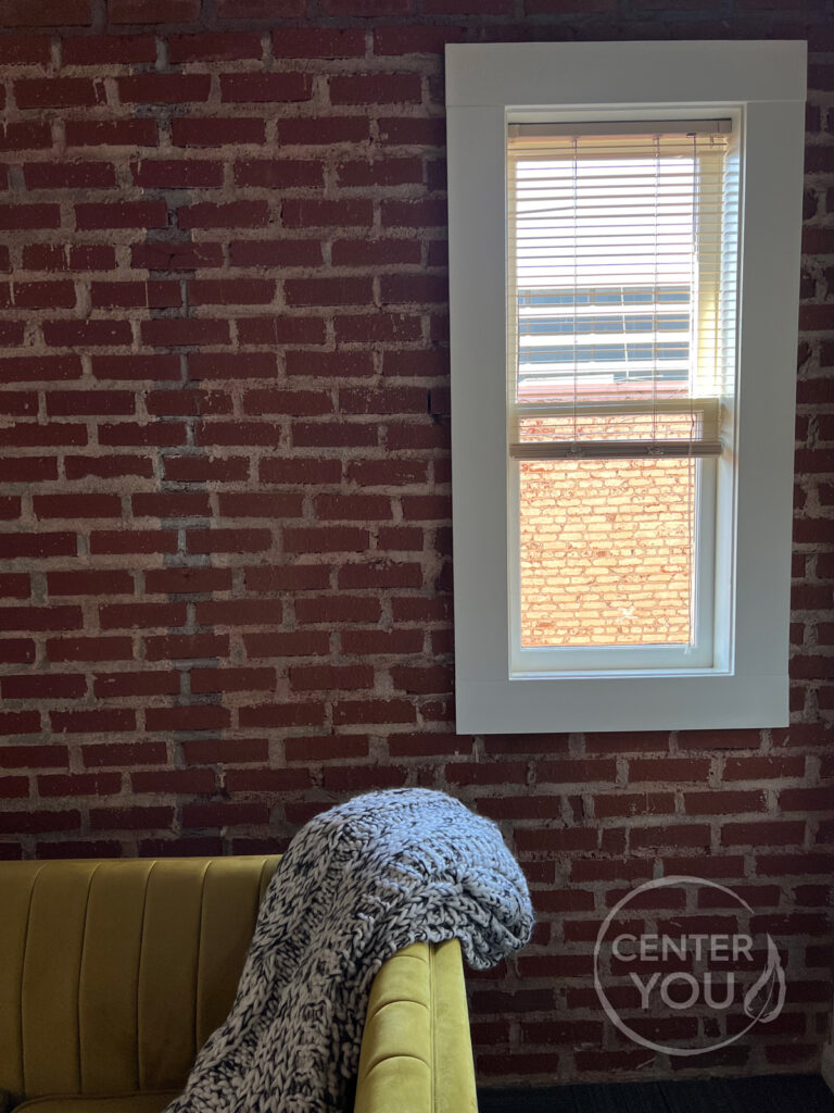 An interior brick wall with a window and a yellow couch.